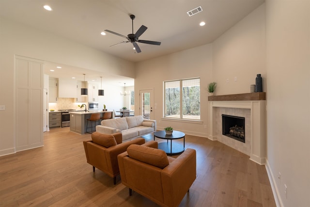 living room featuring light wood-style flooring, a fireplace, visible vents, and a ceiling fan