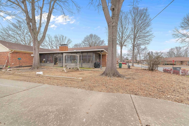 view of front of home featuring a sunroom, brick siding, and a chimney