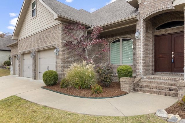 doorway to property with a shingled roof, brick siding, driveway, and a garage