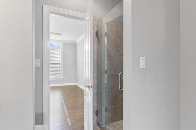 bathroom featuring ornamental molding, wood finished floors, a shower stall, and baseboards