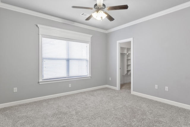 carpeted empty room with a ceiling fan, visible vents, baseboards, and crown molding