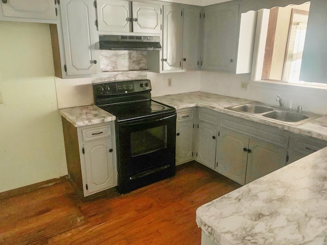 kitchen featuring black range with electric cooktop, under cabinet range hood, a sink, light countertops, and dark wood-style floors