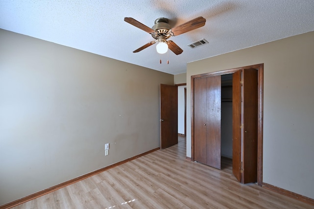 unfurnished bedroom featuring a closet, baseboards, a textured ceiling, and light wood finished floors