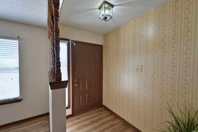 entrance foyer featuring light wood-type flooring, wallpapered walls, baseboards, and a textured ceiling