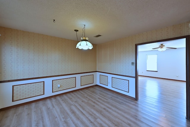 empty room with visible vents, a textured ceiling, and wallpapered walls