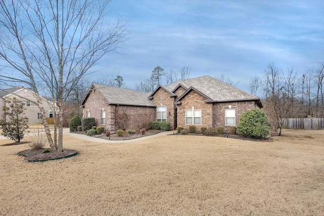 view of front of house featuring a front yard, fence, brick siding, and roof with shingles