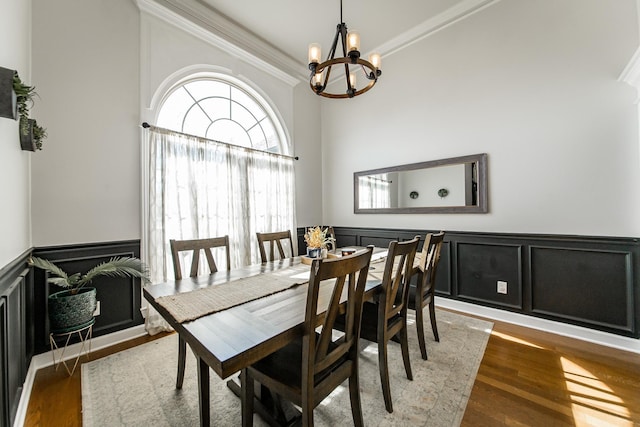 dining space featuring a wainscoted wall, ornamental molding, wood finished floors, an inviting chandelier, and a decorative wall