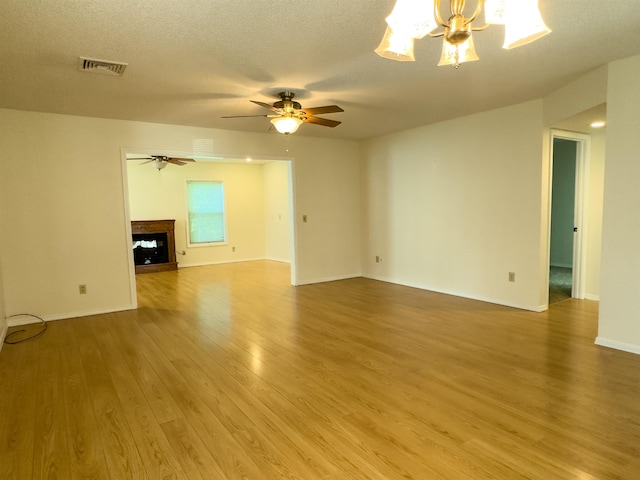 unfurnished living room featuring a fireplace, visible vents, a textured ceiling, wood finished floors, and ceiling fan with notable chandelier