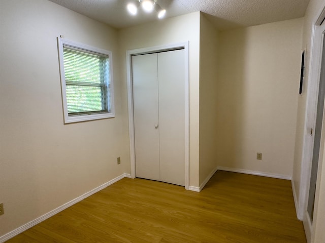 unfurnished bedroom featuring a textured ceiling, a closet, light wood-style flooring, and baseboards