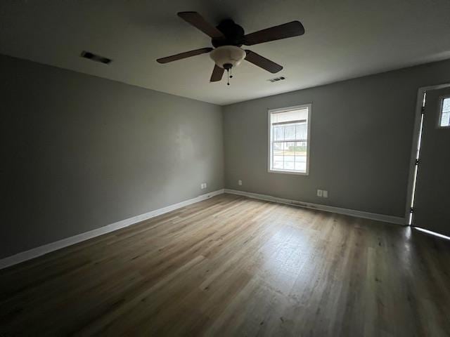 unfurnished room with baseboards, visible vents, ceiling fan, and dark wood-type flooring