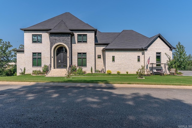 french country style house featuring a front lawn and a shingled roof