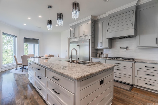 kitchen featuring built in fridge, light stone counters, black gas cooktop, a kitchen island with sink, and a sink