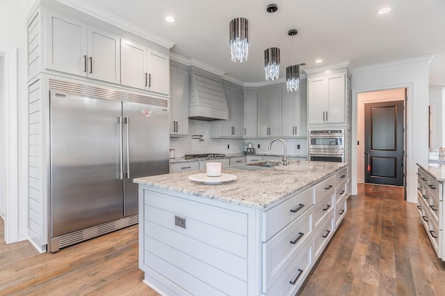 kitchen featuring light stone counters, a sink, appliances with stainless steel finishes, custom exhaust hood, and pendant lighting