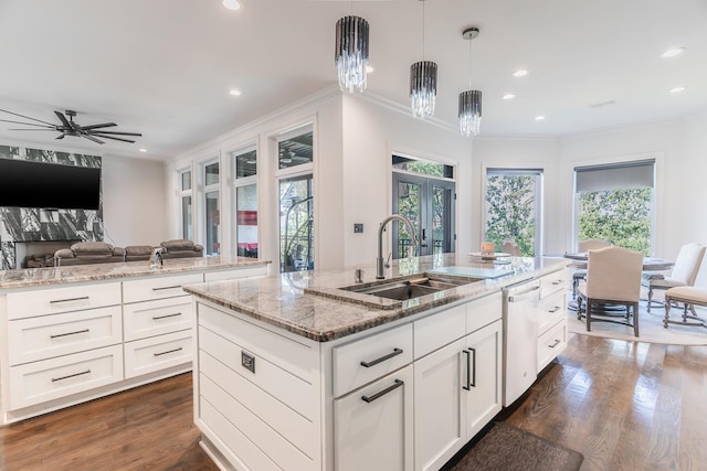 kitchen featuring hanging light fixtures, light stone countertops, a kitchen island with sink, and white cabinets