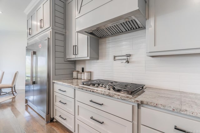 kitchen featuring tasteful backsplash, custom range hood, appliances with stainless steel finishes, white cabinetry, and light stone countertops