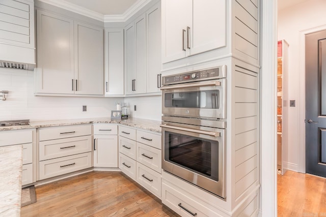 kitchen with double oven, light wood-style flooring, and light stone countertops