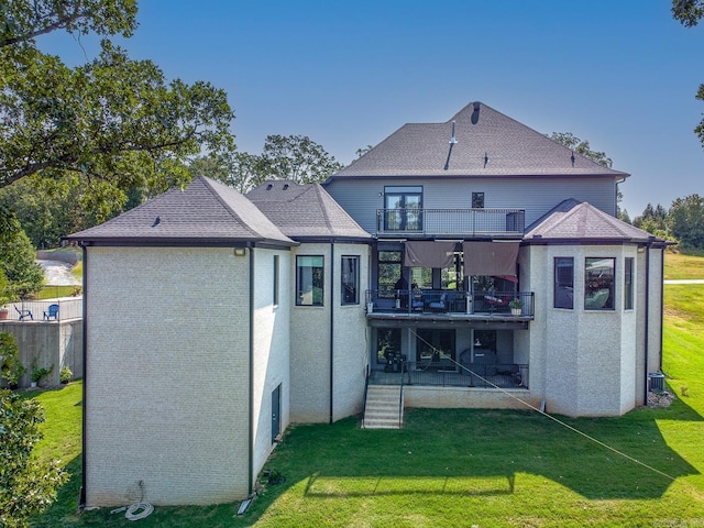 rear view of property featuring a balcony, a shingled roof, and a yard