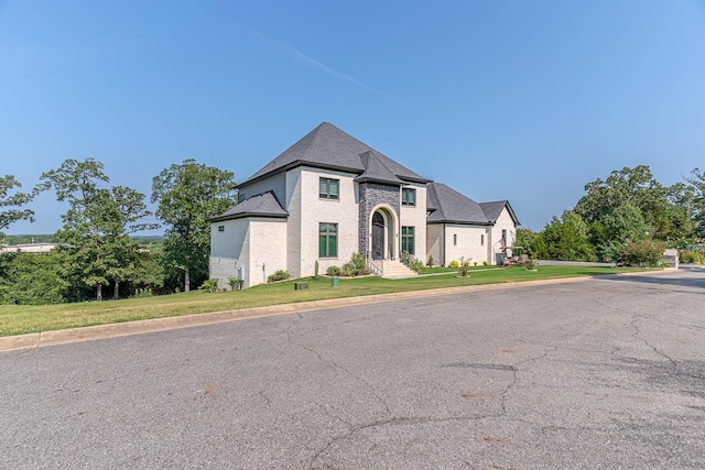 french country inspired facade featuring brick siding and a front yard