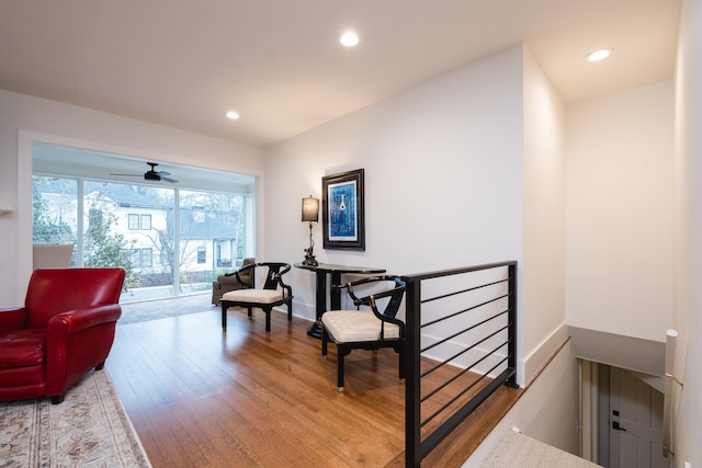 sitting room with recessed lighting, baseboards, wood finished floors, and an upstairs landing