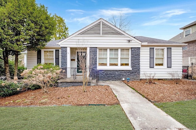 bungalow-style house featuring a shingled roof, a front yard, and stone siding