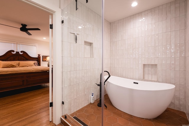 ensuite bathroom featuring tile walls, a stall shower, ensuite bath, wood finished floors, and a freestanding tub