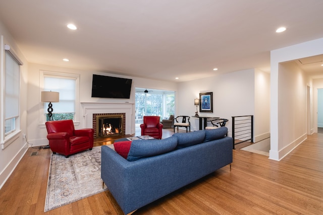 living area with baseboards, light wood-type flooring, a fireplace, and recessed lighting