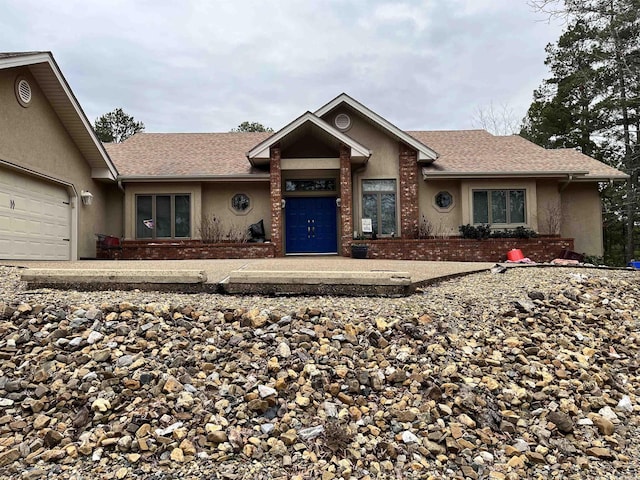 ranch-style home featuring brick siding, roof with shingles, an attached garage, and stucco siding