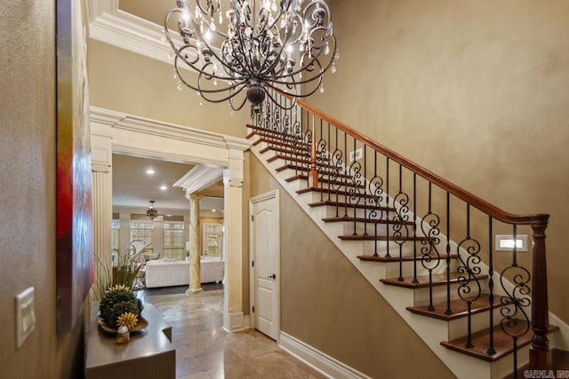 stairs featuring decorative columns, baseboards, ornamental molding, a high ceiling, and ceiling fan with notable chandelier