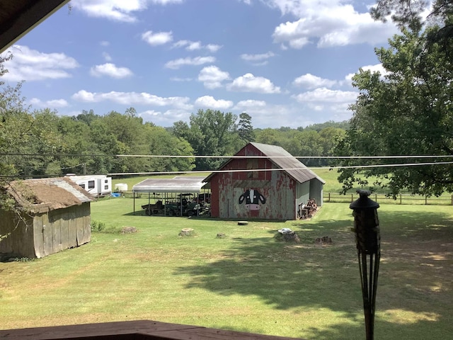 view of yard with a carport, a barn, a wooded view, and an outdoor structure