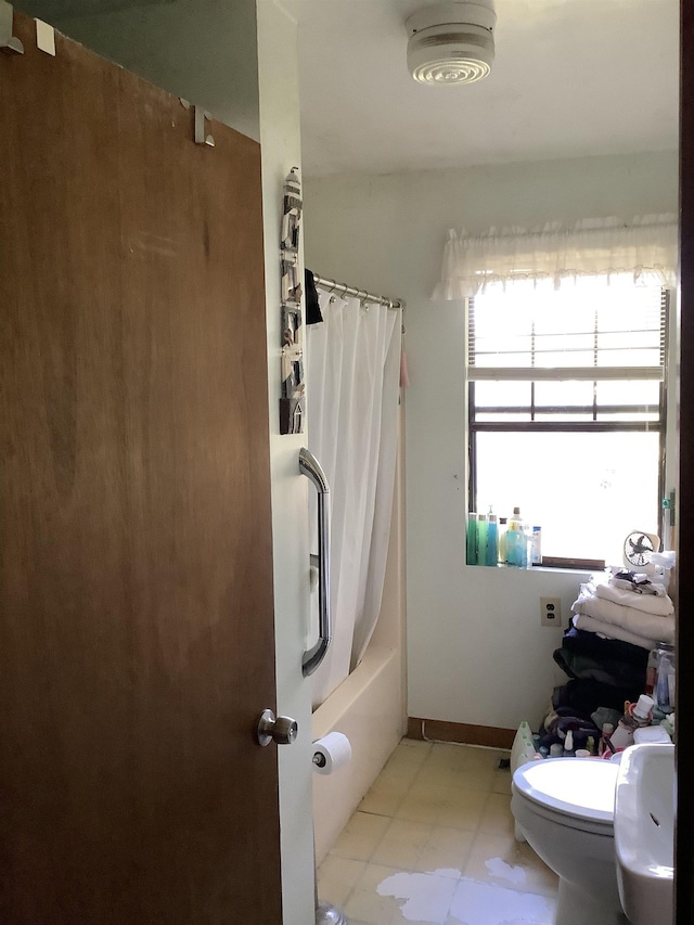 bathroom featuring shower / bath combination with curtain, toilet, and baseboards