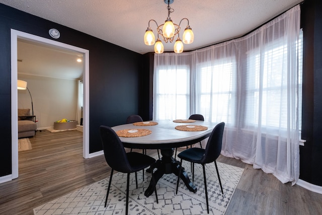 dining area with a chandelier, a textured ceiling, baseboards, and wood finished floors