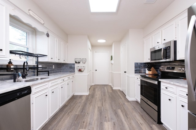 kitchen featuring white cabinetry, appliances with stainless steel finishes, light wood-style flooring, and a sink