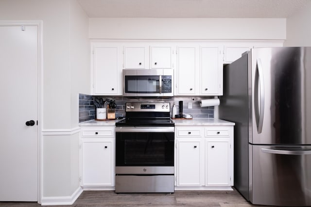 kitchen with appliances with stainless steel finishes, light countertops, white cabinetry, and wood finished floors