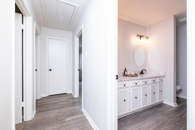 hallway with attic access, a sink, baseboards, and wood finished floors