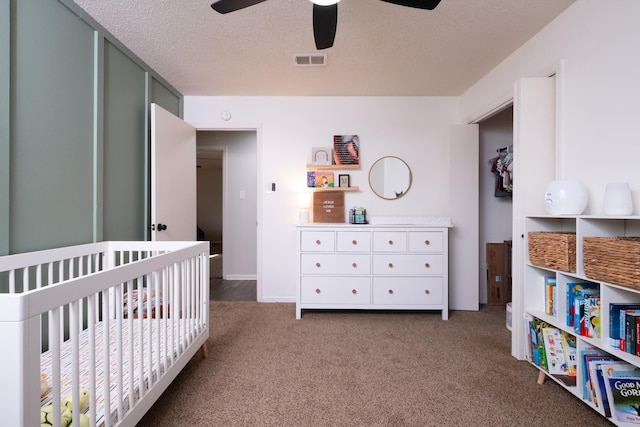 carpeted bedroom featuring a textured ceiling, ceiling fan, visible vents, baseboards, and a crib