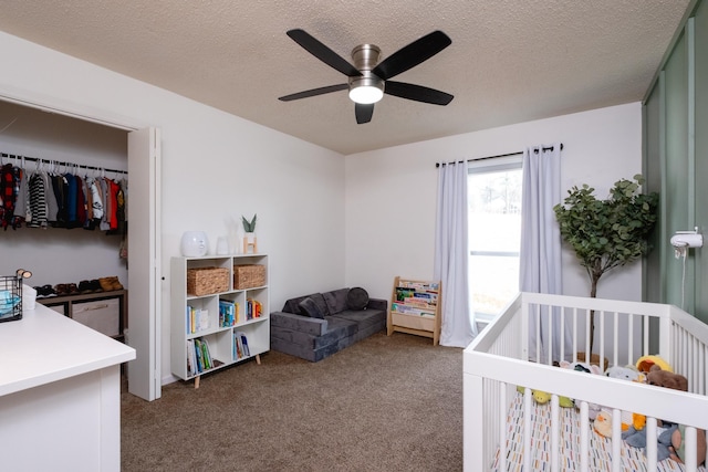 carpeted bedroom featuring a textured ceiling, ceiling fan, and a crib