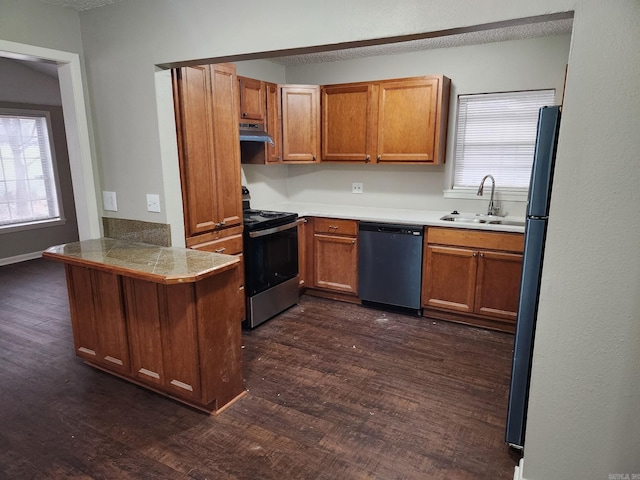 kitchen featuring tile countertops, appliances with stainless steel finishes, brown cabinets, under cabinet range hood, and a sink