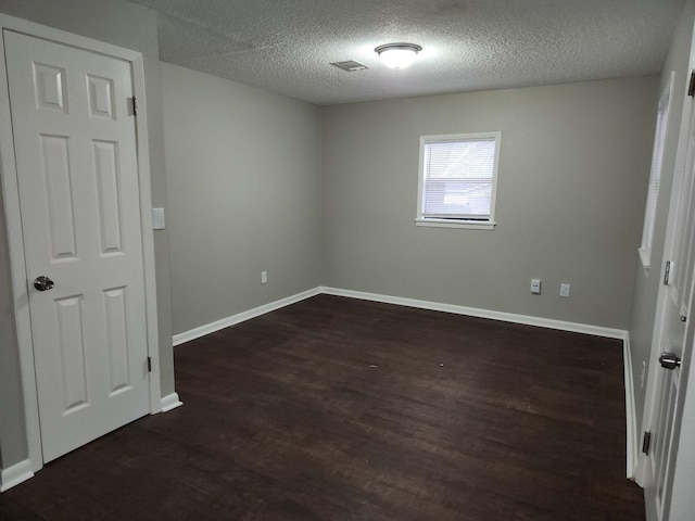 unfurnished bedroom with a textured ceiling, dark wood-style flooring, visible vents, and baseboards