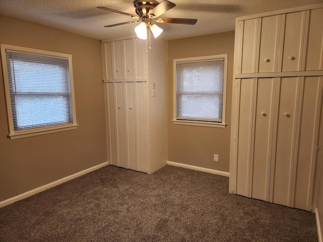 unfurnished bedroom featuring multiple windows, dark colored carpet, and a textured ceiling