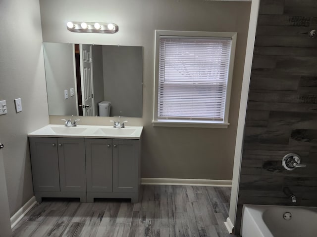 full bath featuring double vanity, baseboards, toilet, wood finished floors, and a sink