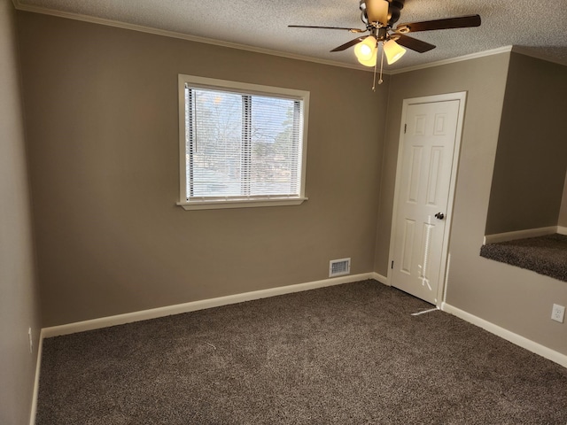 empty room with a textured ceiling, visible vents, baseboards, dark carpet, and crown molding