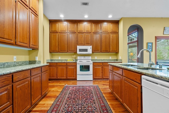 kitchen with white appliances, a sink, visible vents, light wood-style floors, and light stone countertops