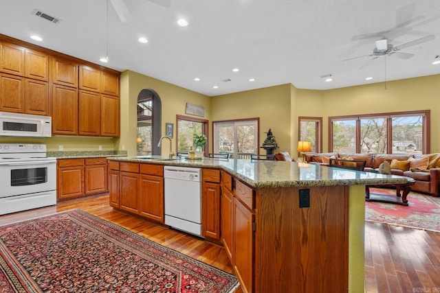 kitchen with white appliances, a sink, a kitchen island, light wood-style floors, and open floor plan