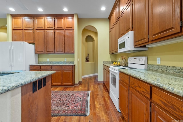 kitchen featuring recessed lighting, white appliances, brown cabinets, light stone countertops, and dark wood finished floors
