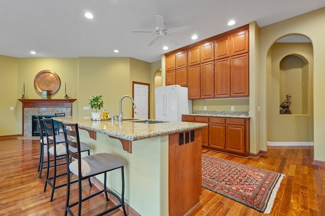 kitchen with a breakfast bar, wood finished floors, a sink, freestanding refrigerator, and an island with sink