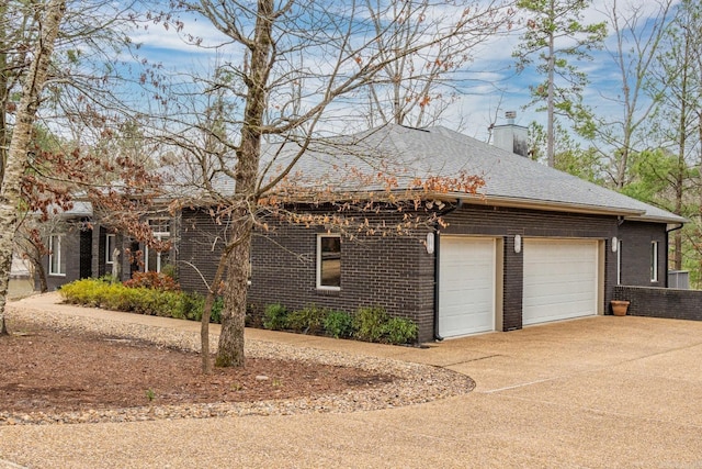 view of side of property with a garage, a shingled roof, concrete driveway, a chimney, and brick siding