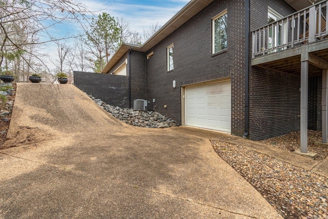 view of home's exterior featuring an attached garage, central AC, concrete driveway, and brick siding