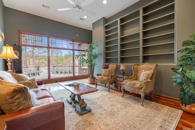 sitting room featuring visible vents, built in features, a ceiling fan, baseboards, and wood finished floors