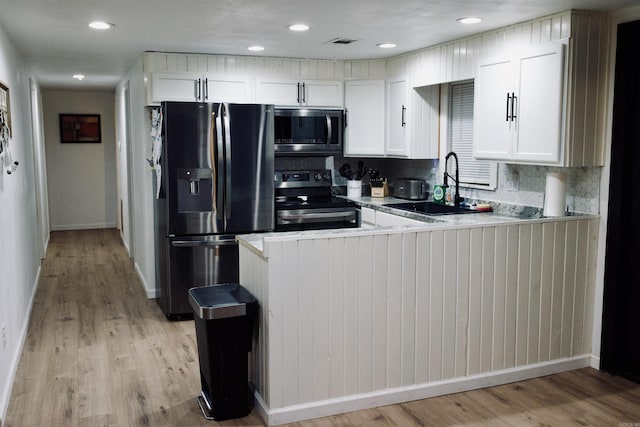 kitchen with white cabinets, a peninsula, stainless steel appliances, light countertops, and a sink