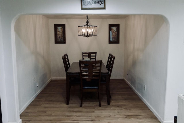 dining space featuring an inviting chandelier, baseboards, arched walkways, and dark wood finished floors